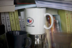 In this Dec. 3, 2018, photo, a cup baring the logo of U.S. Meat Export Federation is placed inside a bookshelf at an office in the Beijing International Club. The Trump administration and China are facing growing pressure to blink in their six-month stare-down over trade because of jittery markets and portents of economic weakness. The longer their trade war lasts, the longer companies and consumers will feel the pain of higher-priced imports and exports.