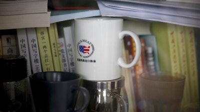 In this Dec. 3, 2018, photo, a cup baring the logo of U.S. Meat Export Federation is placed inside a bookshelf at an office in the Beijing International Club. The Trump administration and China are facing growing pressure to blink in their six-month stare-down over trade because of jittery markets and portents of economic weakness. The longer their trade war lasts, the longer companies and consumers will feel the pain of higher-priced imports and exports.