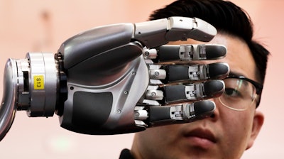 In this Aug. 23, 2017, file photo, a visitor looks at a robotic hand powered by Kinfinity Glove, developed by the German Aerospace Center, on display at the World Robot Conference at the Yichuang International Conference and Exhibition Centre in Beijing. China’s government has appealed to Washington to accept its industrial progress after U.S. intelligence officials said Beijing helps to steal and copy foreign technologies.