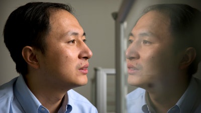 In this Oct. 10, 2018, file photo, He Jiankui is reflected in a glass panel as he works at a computer at a laboratory in Shenzhen in southern China's Guangdong province. A Chinese investigation says Chinese scientist He, behind the reported birth of two babies whose genes had been edited in hopes of making them resistant to the AIDS virus, acted on his own and will be punished for any violations of the law.
