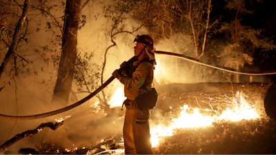 In this Oct. 14, 2017 file photo, a firefighter holds a water hose while fighting a wildfire in Santa Rosa, Calif. Investigators say the deadly 2017 wildfire that killed 22 people in California's wine country was caused by a private electrical system, not embattled Pacific Gas & Electric Co. The state's firefighting agency said Thursday, Jan. 24, 2019, that the Tubbs Fire started next to a residence. They did not find any violations of state law.