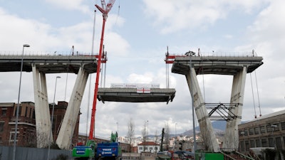 Cranes lower a section of the Morandi bridge in Genoa, Italy, Saturday, Feb. 9, 2019. Workers taking apart the remains of a bridge which collapsed in Aug. 2018 are set to remove a 40 meter beam, seen in between the red machinery. A large section of the bridge collapsed over an industrial area in the Italian city of Genova last summer during a sudden and violent storm, leaving vehicles crushed in rubble below and killing 43 people.