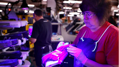 In this Dec. 17, 2018 photo, Laurie French applies adhesive under an ultraviolet light to a pair of athletic shoes designed for the military at a New Balance factory in Norridgewock, Maine. On Friday, Feb. 15, 2019, the Federal Reserve reports on U.S. industrial production for January.