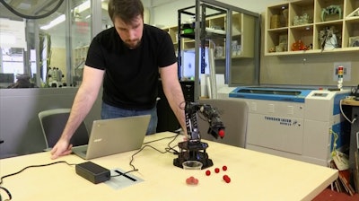Robert Kwiatkowski, a graduate student at Columbia University, demonstrates a robotic arm picking up a red ball and dropping it in a cup at the school in New York. Columbia University engineers have given a robot the ability to model itself without prior knowledge of physics or its own shape.