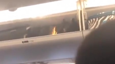 A screenshot taken from a video posted online right before a flight attendant uses a fire extinguisher on a flaming bag.