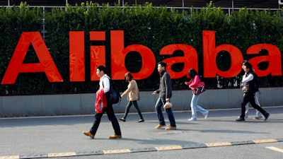 In this March 17, 2014 file photo, people walk past a company logo at the Alibaba Group headquarters in Hangzhou, in eastern China's Zhejiang province. Office Depot and Alibaba.com are creating a co-branded online store to expand the reach of both companies with small and medium size businesses. The two companies announced the agreement Monday, March 4, 2019, as part of a broader array of services they are providing to small business. Over time, the companies intend to help U.S. small businesses sell their products to buyers around the world through Alibaba.com. It marks Alibaba.com’s first U.S. partnership with a major company.