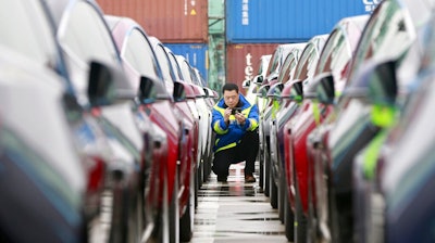 In this Feb. 22, 2019, photo, a port worker works among one of the first batches of Tesla Model 3 electric cars to be delivered to China at a port in Shanghai. In an unusual step, China’s ceremonial legislature is due to endorse a law meant to help end a bruising tariff war with Washington by discouraging officials from pressuring foreign companies to hand over technology.