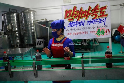A worker runs a conveyor belt moving bottles of soft drinks near a propaganda banner that reads 'Let's uphold the banner of the speed of Mallima (a mythical Pegasus-type horse)' at Kumkhop Trading Co. food factory in Pyongyang, North Korea.
