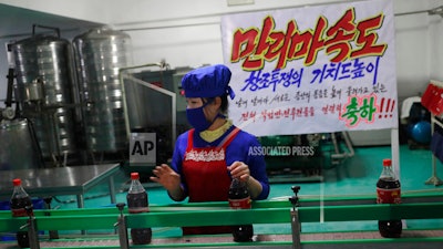 A worker runs a conveyor belt moving bottles of soft drinks near a propaganda banner that reads 'Let's uphold the banner of the speed of Mallima (a mythical Pegasus-type horse)' at Kumkhop Trading Co. food factory in Pyongyang, North Korea.