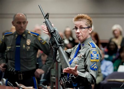 In this Jan. 28, 2013, file photo, firearms training unit Detective Barbara J. Mattson, of the Connecticut State Police, holds a Bushmaster AR-15 rifle, the same make and model used by Adam Lanza in the 2012 Sandy Hook School shooting, during a hearing at the Legislative Office Building in Hartford, Conn. A divided Connecticut Supreme Court ruled, Thursday, March 14, 2019, gun maker Remington can be sued over how it marketed the Bushmaster rifle used in the massacre.