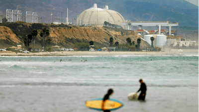 In this June 7, 2013 file photo surfers stand in water in front of the shuttered San Onofre Nuclear Generating Station in San Onofre, Calif. The Nuclear Regulatory Commission is fining Southern California Edison $116,000 for violations in its handling of nuclear canisters at the facility. The decision announced Monday, March 25, 2019, in an online town hall meeting involves the transfer of radioactive nuclear waste containers from cooling pools to safer bunkers. The Orange County Register reports Southern California Edison indicated it would accept the penalty.