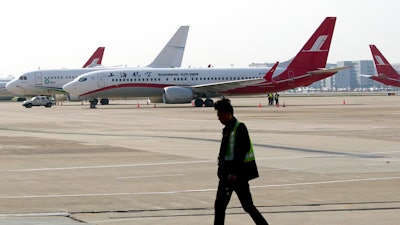 A ground crew walks near a Boeing 737 Max 8 plane operated by Shanghai Airlines parked on the tarmac at Hongqiao airport in Shanghai, China, Tuesday, March 12, 2019. U.S. aviation experts on Tuesday joined the investigation into the crash of an Ethiopian Airlines jetliner that killed 157 people, as a growing number of airlines grounded the new Boeing plane involved in the crash.