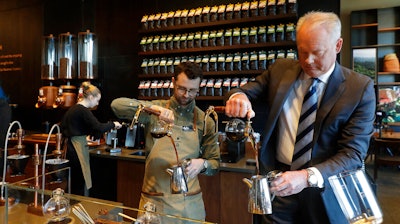 In this March 5, 2019, photo Kevin Johnson, right, CEO of Starbucks, makes coffee using a siphon method alongside barista Dylan George, left, as Johnson visits the company's Starbucks Reserve store in the company's headquarters building in Seattle's SODO neighborhood.