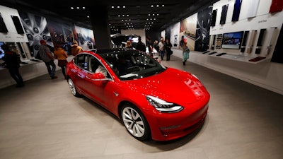 In this Feb. 9, 2019, file photograph, buyers look over a Model 3 in a Tesla store in Cherry Creek Mall in Denver. Tesla is shifting all of its sales from stores to the internet, saying the move is needed to cut costs so it can sell the mass-market Model 3 for a starting price of $35,000. The Palo Alto, California, company announced the change Thursday, Feb. 28.