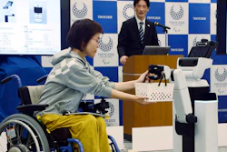 A robot passes a basket containing drinks to a woman in wheelchair during an unveiling event in Tokyo Friday, March 15, 2019. Organizers on Friday showed off robots that will be used at the new National Stadium to provide assistance for fans using wheelchairs.