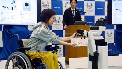 A robot passes a basket containing drinks to a woman in wheelchair during an unveiling event in Tokyo Friday, March 15, 2019. Organizers on Friday showed off robots that will be used at the new National Stadium to provide assistance for fans using wheelchairs.