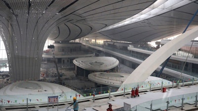 Workers past through the terminal of the Beijing Daxing International Airport under construction on the outskirts of Beijing, China, Friday, March 1, 2019. Construction on the new airport in China's capital which promises to be one of the world's largest is speeding toward completion.