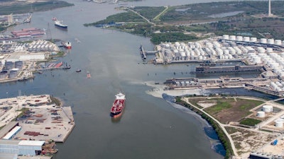 In a Wednesday, March 20, 2019 photo, maritime traffic moves through the Houston Ship Chanel past the site of now-extinguished petrochemical tank fire at Intercontinental Terminals Company in Deer Park, Texas. Air quality and water pollution from the fire's runoff, seen on the right, into the ship channel are some of the concerns in the aftermath of the blaze.