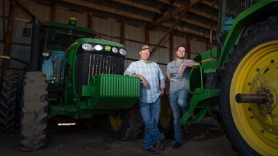 In this Friday, March 15, 2019 photo, Grant Cummins and his son Parker have their photo taken with some of the tractors they use to farm mint near Murtaugh, Idaho. Extracting oil from the peppermint crop is only part of Cummins' business. Cummins, Chad Neeley, president of the Idaho Mint Growers Association said, is one mint grower who has gone 'all in' by growing and selling certified rootstock in addition to producing oil.