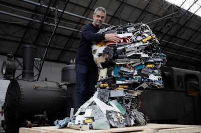 In this picture taken on Thursday, April 11, 2019, designer Piet Hein Eek poses next to his creation 'Electronic Man', made with recycled plastic pieces of variuos electronic devices, during the 'RO Master's Pieces exhibition', on the sidelines of the Salone del Mobile International Furniture Fair week, in Milan, Italy. Scientists and environmental activists have been long raised the alarm on plastic pollution. Now, the high-end design world is getting in on the growing global effort to tackle plastic pollution -- by upcycling discarded objects into desirable one-off design pieces.