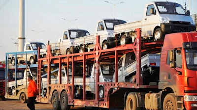 In this Oct. 31, 2018, file photo, a staff member walks past an auto transport loaded with new vehicles in the parking lot for a local automaker in Qingdao in eastern China's Shandong province. The China Association of Auto Manufacturers, reported Friday, April 12, 2019, that sales of SUVs, sedans and minivans in the industry's biggest global market fell 6.9 percent in March from a year earlier.
