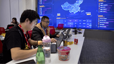 In this Nov. 11, 2018, file photo, workers use their laptops near a display showing sales data at the command center at the headquarters of an e-commerce retailer in Beijing. Remarks by the head of Chinese online business giant Alibaba that young people should work 12-hour days, six days a week if they want financial success have prompted a public debate over work-life balance in the country.