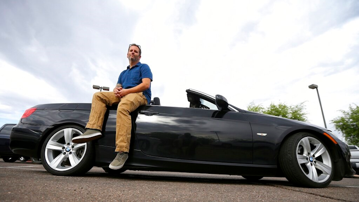 In this April 23, 2019, photo, Chris Williamson poses for a photo sitting on his car in Phoenix. When Williamson was in the market for a new family car, a timely ad and conversations with a co-worker convinced him to try something out of the ordinary. He bought the BMW 3 Series convertible and covers the payments by renting it to strangers on a peer-to-peer car sharing app called Turo. It allows his family of seven to have a nicer car, essentially for free.