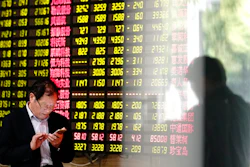 A man looks at his smartphone near a display showing stock prices at a brokerage house in Shanghai Monday, May 6, 2019. China's benchmark Shanghai Composite index dives on U.S. President Donald Trump threat of more China tariffs. At right is a reflection off a display board.