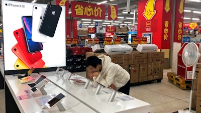 A man browses an iPhone unit on display at a section selling Apple's products together with Chinese made electric appliances at a hypermarket in Beijing, Thursday, May 9, 2019. Ratcheting up tension ahead of talks in Washington, China vowed Thursday to defend its own interests and retaliate if President Donald Trump goes ahead with more tariff hikes in a dispute over trade and technology.