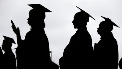 In this May 17, 2018, file photo, new graduates line up before the start of the Bergen Community College commencement at MetLife Stadium in East Rutherford, N.J. A college degree has long been a ticket to the U.S. middle class. Yet a new survey shows that college graduates aren’t as likely as they once were to feel they belong to the middle class.