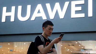 In this Monday, May 20, 2019, photo, a man uses his smartphone outside a Huawei store in Beijing. Chinese tech giant Huawei has filed a motion in U.S. court challenging the constitutionality of a law that limits its sales of telecom equipment.