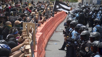 Demonstrators holding wooden shields are confronted by police during a protest against the Federal Fiscal Control Board, as part of the May Day celebration in San Juan, Puerto Rico, Wednesday, May 1, 2019. The U.S. Congress established the appointed Fiscal Control Board to oversee the debt restructuring in order to combat the Puerto Rican government-debt crisis.