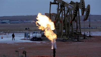 In this Oct. 22, 2015 file photo, workers tend to oil pump jacks behind a natural gas flare near Watford City, N.D. Natural gas is being burned off and wasted at record levels in North Dakota because development of the pipelines and processing facilities needed to handle it has not kept pace. Natural gas production hit a record in March. But about 20 percent of it went up in flames through “flaring,” the process of burning off the gas when it can’t be captured.