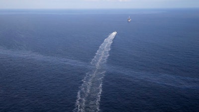 In this March 31, 2015 file photo, the wake of a supply vessel heading towards a working platform crosses over an oil sheen drifting from the site of the former Taylor Energy oil rig in the Gulf of Mexico, off the coast of Louisiana. The Coast Guard says a newly installed containment system is collecting oil at the site of the 14-year-old oil leak in the Gulf of Mexico. A Coast Guard statement Thursday, May 16, 2019, describes the installation of the subsea containment system as a “major milestone” in the federal government’s long-running efforts to contain the leak.