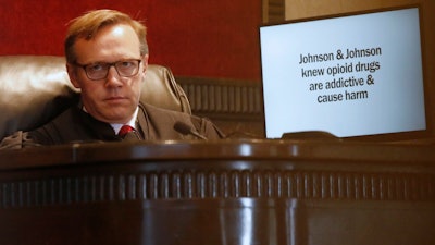 Judge Thad Balkman listens during opening arguments for the state of Oklahoma Tuesday, May 28, 2019, in Norman, Okla., as the nation's first state trial against drugmakers blamed for contributing to the opioid crisis begins in Oklahoma. At right is a slide from the state's presentation shown on a monitor.