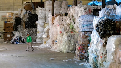 In this May 7, 2019 photo, a man walks under towers of recyclables at a GDB International warehouse in Monmouth Junction, N.J. A decision by China’s government to restrict imports of wastepaper and plastic that has disrupted U.S. recycling programs has also spurred investment in American plants that process recyclables.
