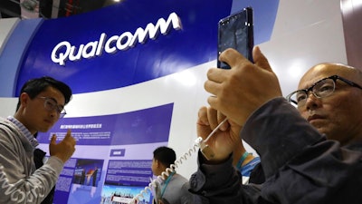 In this Nov. 6, 2018 file photo, attendees look at the latest technology from Qualcomm at the China International Import Expo in Shanghai. Qualcomm’s stock is tumbling before Wednesday’s market open on May 22, 2019, after a federal judge ruled that the company unlawfully stifled cellphone chip market competition and charged excessive licensing fees.