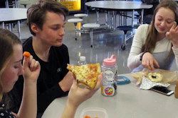 Burlington High School student Emma McCobb, left, holds a piece of pizza while eating with classmates in the school cafeteria in Burlington, VT. The school's food service provider is preparing to comply with a Trump administration decision to roll back a rule that required only whole-grain rich foods for school meals.