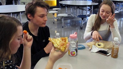 Burlington High School student Emma McCobb, left, holds a piece of pizza while eating with classmates in the school cafeteria in Burlington, VT. The school's food service provider is preparing to comply with a Trump administration decision to roll back a rule that required only whole-grain rich foods for school meals.