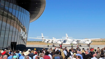In this Oct. 17, 2011, file photo a crowd gathers outside Spaceport America for a dedication ceremony as Virgin Galactic's mothership WhiteKnightTwo sits on the tarmac near Upham, N.M. British billionaire Richard Branson is taking another concrete step toward offering rides into the close reaches of space for paying passengers. Branson announced Friday, May 10, 2019, that Virgin Galactic will immediately begin shifting operations from California to a spaceport and specialized runway in the New Mexico desert in final preparations for commercial flights. He says Virgin Galactic's development and testing program has advanced enough to make the move, which will continue through the summer.