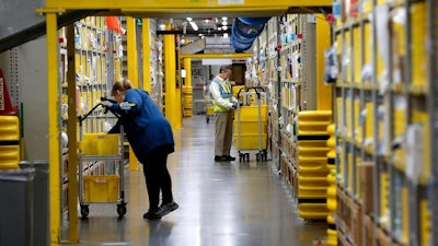 In this Tuesday, May 7, 2019, photo Brooke Pizzetti, left, Grant Frith work at the Amazon Chester Fulfillment Center in Chester, Va.