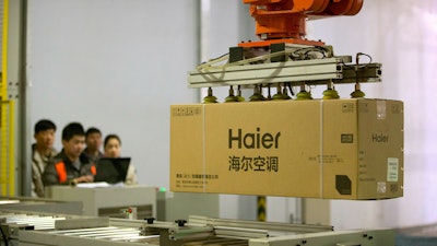 In this Feb. 24, 2017, file photo, factory workers watch as a machine uses suction to lift a box containing an air conditioner at a Haier factory in Jiaozhou near Qingdao in eastern China's Shandong Province. For months, the U.S. economy has shrugged off the tariffs slapped by America and China on tens of billions of dollars of each other’s goods. The higher duties would cover thousands of Chinese imports, from refrigerators, air conditioners and washing machines to bamboo mats, microphones and cigarette paper.