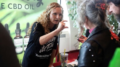 In this April 7, 2019 photo, Lindsey Bouras, left, wellness consultant at The Healthy Place, formerly known as Apple Wellness, talks to an attendee about CBD oil at the, It's Hemp, It's Fine hemp/CBD event, at Monona Terrace Convention Center in Madison, Wisc. The event featured a panel discussion, informational booths, and free samples of CBD coffee, beer, kombucha, candy and more.