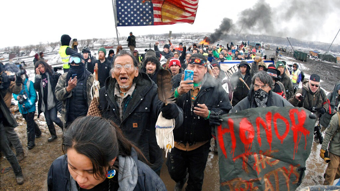 In this Feb. 22, 2017, file photo, a large crowd representing a majority of the remaining Dakota Access Pipeline protesters march out of the Oceti Sakowin camp before the deadline set for evacuation of the camp mandated by the U.S. Army Corps of Engineers near Cannon Ball, N.D. North Dakota's congressional delegation is urging two Trump administration officials to address the state's year-old demand for $38 million to cover the cost of policing large-scale and at times violent protests against the Dakota Access oil pipeline.
