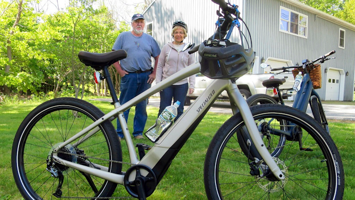 In this June 8, 2019 photo, Gordon and Janice Goodwin show their electric-assist bicycles outside their home in Bar Harbor, Maine. The bikes are banned on carriage roads and bicycle paths in nearby Acadia National Park.