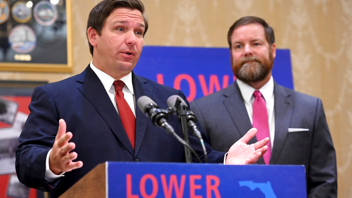 Florida Gov. Ron DeSantis speaks about the need to lower prescription costs by importing drugs from other countries, Tuesday, June 11, 2019, at the Eisenhower Recreation Center in The Villages, Fla. Listening at right is state Sen. Aaron Bean.