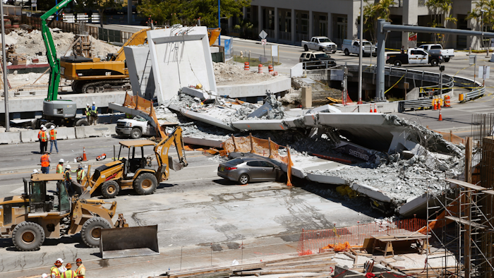 In this March 16, 2018 file photo crushed cars are shown under a section of a collapsed pedestrian bridge near Florida International University in the Miami area. A federal workplace safety agency says engineers had knowledge of extensive cracking and failed to order to close a street and shore up a pedestrian bridge before it collapsed and killed six people at a Miami university last year. On Tuesday, June 11, 2019 a report by the U.S. Occupational Safety and Health Administration concluded the size of the cracks warranted the street be shut down immediately.