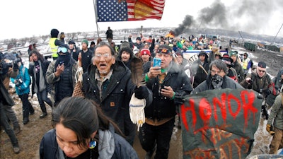 In this Feb. 22, 2017, file photo, a large crowd representing a majority of the remaining Dakota Access Pipeline protesters march out of the Oceti Sakowin camp before the deadline set for evacuation of the camp mandated by the U.S. Army Corps of Engineers near Cannon Ball, N.D. North Dakota's congressional delegation is urging two Trump administration officials to address the state's year-old demand for $38 million to cover the cost of policing large-scale and at times violent protests against the Dakota Access oil pipeline.