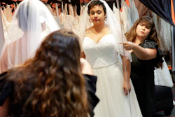 In this Friday, June 21, 2019, photo Ann Campeau,, right, owner of Strut Bridal, fits a new dress on inventory manager Stefanie Zuniga at her shop in Tempe, Ariz. Cut-rate prices on websites that sell wedding dresses direct from China put pressure on Campeau, who owns four bridal shops in California and Arizona. She has had customers come in after seeing low-end gowns online and expecting to get a dress at a similar price.