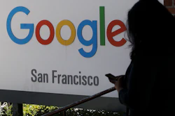 In this May 1, 2019, file photo, a woman walks past a Google sign in San Francisco. The U.S. Justice Department and the Federal Trade Commission are moving to investigate Google, Facebook, Amazon and Apple over their aggressive business practices, and the House Judiciary Committee has announced an antitrust probe of unidentified technology companies.